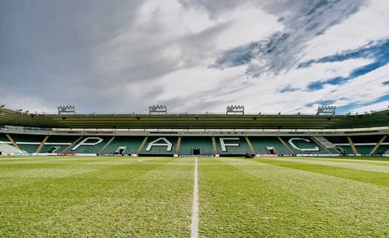 Home Park, the stadium of Plymouth Argyle F.C. The Lyndhurst stand is visible, featuring dark green seats, with a pattern of white seats spelling out the letters PAFC.