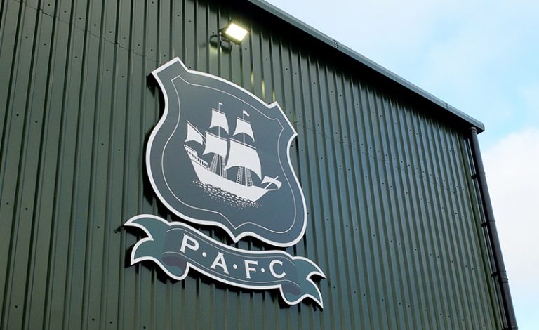 Home Park, the stadium of Plymouth Argyle F.C. The outside of the Mayflower stand is pictured, including the Plymouth Argyle badge, featuring the Mayflower ship emblem.